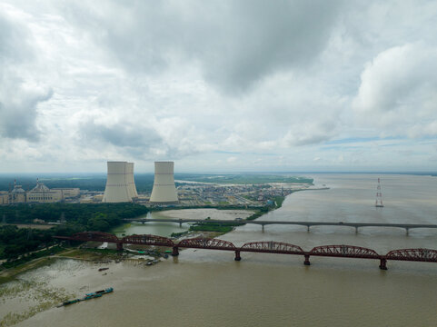 Aerial view of the towering nuclear reactors and a long bridge over a wide river under a cloudy sky, Ruppur, Rajshahi Division, Bangladesh.