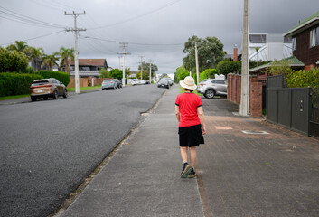 Woman walking on the roadside pedestrian footpath in an Auckland suburb. Cars parked along the street.