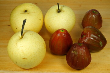Three pears or Pyrus communis and four overripe water apples on a wooden base taken from three quarter angle.