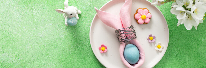 A beautifully arranged table setting for Easter features a pink napkin wrapped around an egg, surrounded by floral decorations and colorful candies, banner