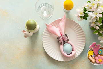 A vibrant Easter table setting features a beautifully arranged plate with a wrapped egg, decorated cookies, and fresh flowers, creating a joyful atmosphere for the holiday gathering