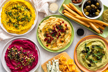 A vibrant spread showcases different types of hummus including classic, beetroot, broccoli, and turmeric. Accompanied by olives and breadsticks, it invites sharing and enjoyment