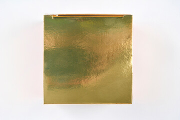 An overhead shot shows the reflective, shimmering surface of a closed square golden gift box centered on a bright white background