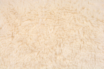 A horizontal full-frame close-up shot of a soft, dense, and textured beige or cream-colored artificial fur fabric