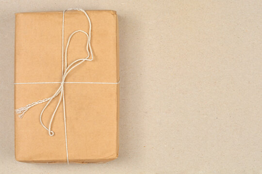 A rectangular brown paper package tied with white string is positioned on the left side of a textured brown cardboard background with ample copy space