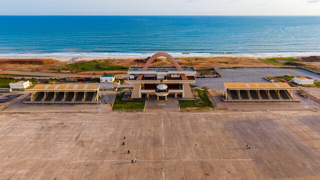 Aerial view of the Black Star Square, a stark contrast between the concrete expanse and the vibrant blue of the Atlantic Ocean, Accra, Ghana.