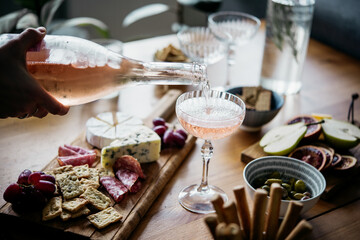 Pouring rose wine with classic snacks of cheese, bread and olives. Party or anniversary celebration.