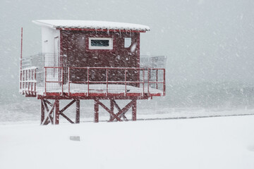 Red lifeguard tower construction on the coast during heavy snowing