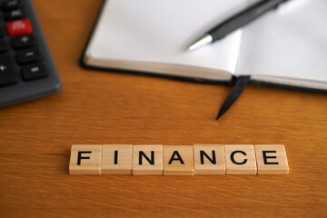 FINANCE. Financial concepts. Wooden letters with calculator and notebook in the background.