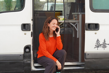 Smiling woman in a red sweater, talking on the phone in her camper van
