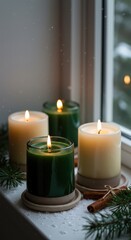Four candles burning by a window with snow and greenery creating a cozy winter atmosphere indoors