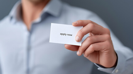 Man in a formal shirt holding a white business card with the words apply now on it, symbolizing a direct invitation for job seekers and career opportunities with copy space