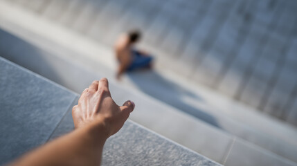 Reaching out for connection, a hand extending towards a lonely, out of focus man sitting on isolated concrete stairs, showing emotional longing and distance with copy space