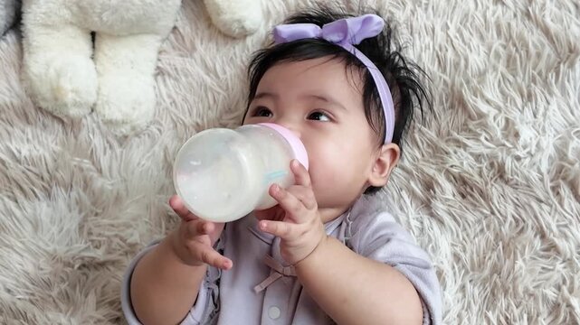 A cute baby girl holding a milk bottle and drinking by herself, showing finger development