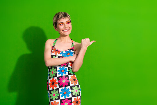 Glamorous young woman in a colorful flower print dress standing against a green background smiling - Powered by Adobe