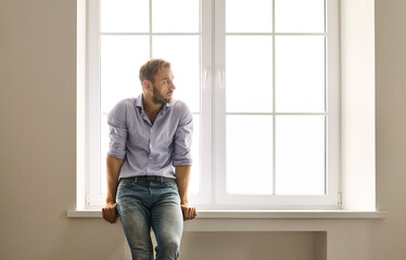 Man by window thinking about depression, anxiety. Soft daylight traces his pensive posture on the...