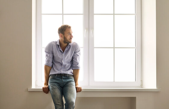 Man by window thinking about depression, anxiety. Soft daylight traces his pensive posture on the sill. He faces stress, solitude, and a health problem. Core concept: mental health struggle.