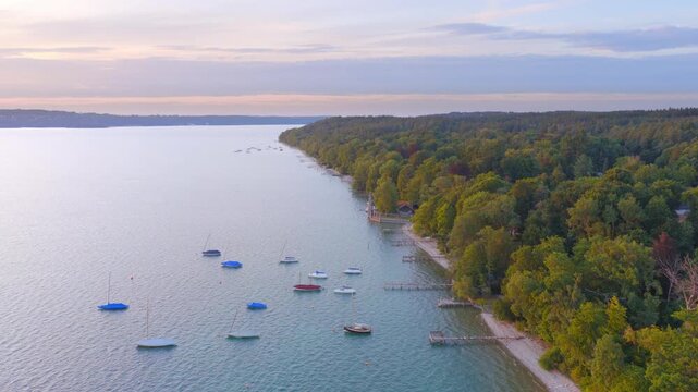 Soft evening light falls over Lake Starnberg. Small boats gently drift on the clear water as the forested shoreline stretches calmly along the coast.