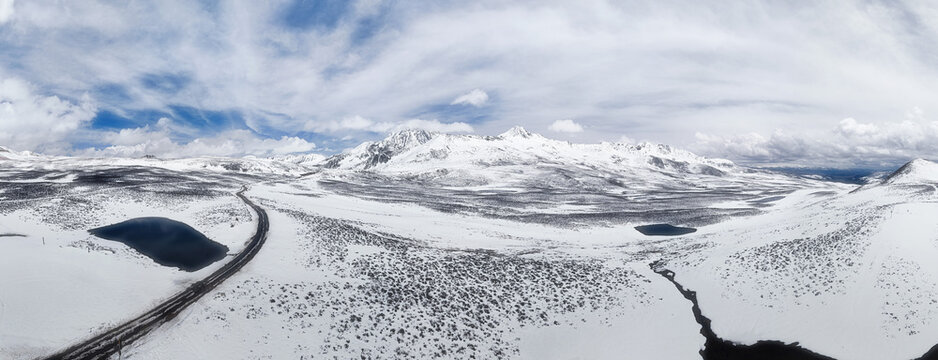 Aerial view of a winding road cuts through a vast, snow-covered landscape, contrasting with the dark waters of a small lake, Wenshan Zhuang and Miao Autonomous Prefecture, China.
