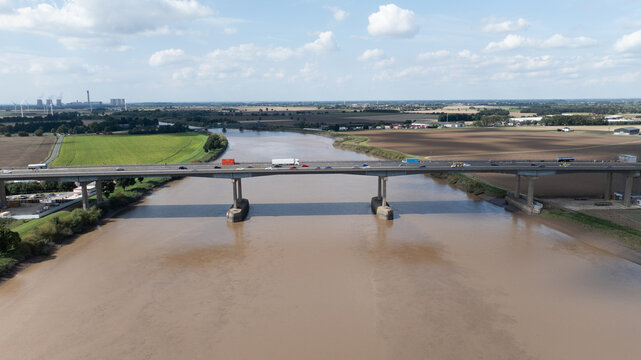 Aerial view of the Ouse Bridge stretching across the muddy river, connecting vibrant green fields with earthy-toned farmlands, Goole, United Kingdom.
