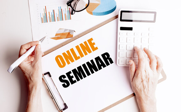 Text online seminar written on clipboard with hands using pen and calculator, charts and glasses on desk