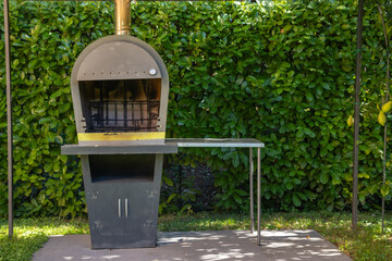 Outdoor pizza oven and barbecue grill with chimney, rustic design for cooking and grilling in a garden setting. Traditional Italian-style outdoor kitchen element