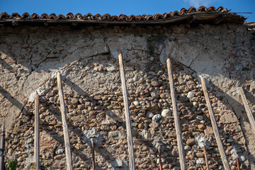 Old stone and mortar wall in disrepair with temporary wooden supports. Rustic texture, weathered masonry, and structural reinforcement in an outdoor setting