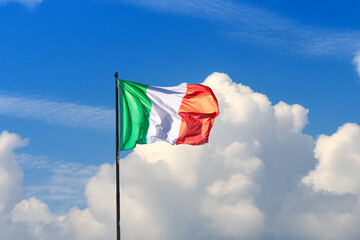 Italian flag waving in the sky on a bright day. National tricolor fluttering against a cloudy blue background, symbolizing Italy, patriotism, and cultural identity