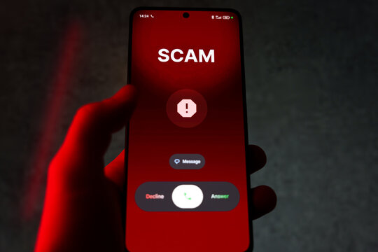 Hand holding smartphone with scam warning and call options on red screen