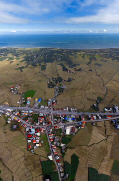 Aerial view of a coastal landscape where the dark blue sea meets the golden fields, divided by a network of roads and clustered buildings, Khotbeh Sara, Talesh, Iran.