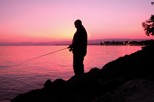 Silhouette d'un homme qui p&ecirc;che &agrave; la ligne sur les berges du lac L&eacute;man, Lausanne, Suisse