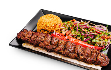 Delicious grilled kebab with rice and fresh salad served on black plate