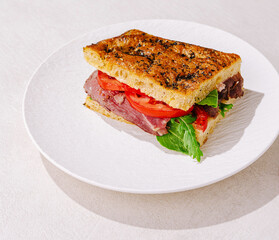Delicious roast beef sandwich with fresh tomatoes and lettuce on a white plate