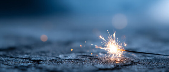 Close-up of a lit sparkler on a textured surface with glowing sparks and blurred blue background creating a festive and celebratory atmosphere