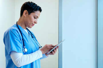 Young woman nurse using digital tablet while standing in medical facility, short hair and stethoscope , focused on screen, professional healthcare setting