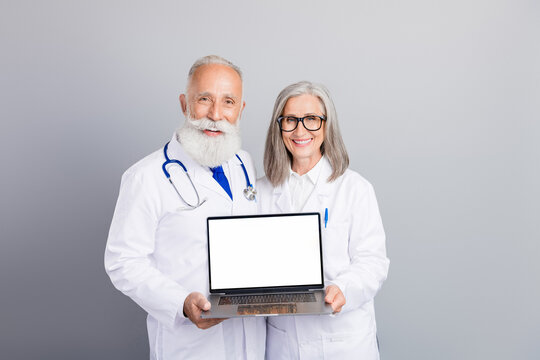 Two doctors in white coats present a laptop with blank screen symbolizing medical consultation and professional care in a calm clinic setting