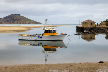 A small fishing boat reflected in calm coastal waters at  Waikouaiti Bay, Otago, New Zealand