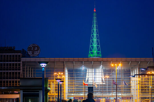Illuminated MTP spire above the glass main entrance facade creating a distinctive nighttime view of Poznań trade fair architecture