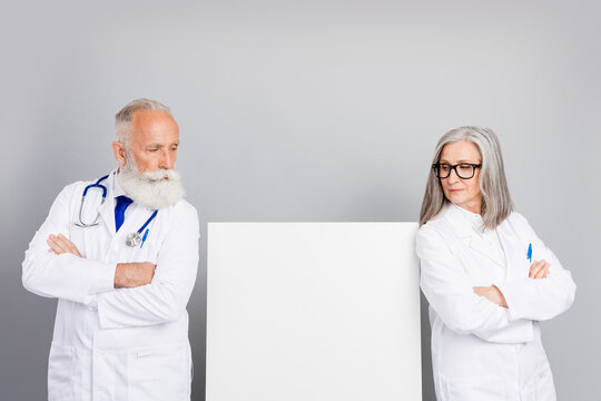 Two experienced doctors in white coats stand on either side of a blank panel as they discuss patient care in a calm clinical setting