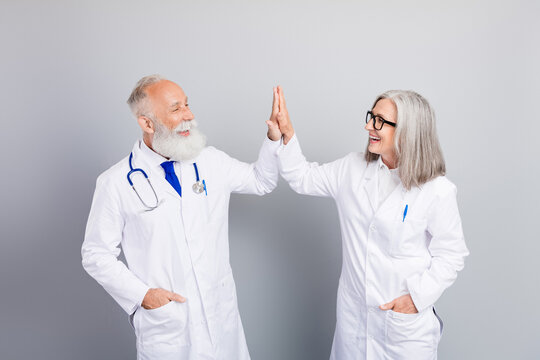 Two experienced doctors high five in white coats celebrate teamwork after a medical consultation and friendly patient care scene