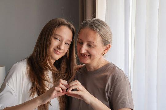 Teen girl and mother making heart gesture after resolving conflict. Sweet reconciliation moment, family love and restored emotional connection
