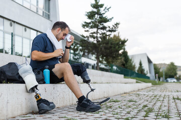 Athlete with leg amputation resting on outdoor steps, wiping sweat during workout pause. Strength, motivation, and healthy living concepts.