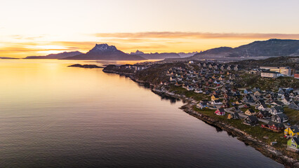 Aerial view of the coastline illuminated by the warm glow of the setting sun, reflecting on the calm waters near the town, Nuuk, Sermersooq Municipality, Greenland.