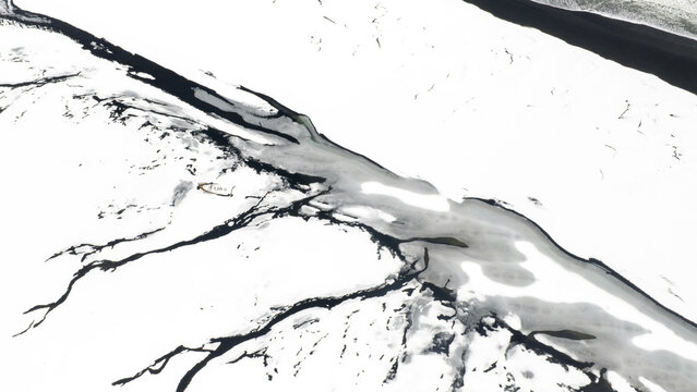 Aerial view of stark, black river channels carve through a brilliant white glacial expanse, creating a dramatic contrast in texture and tone, Vik, Iceland.