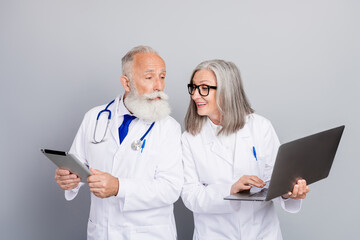 Two experienced doctors aged colleagues discuss patient care using tablet laptop in coats in hospital clinic photograph teamwork dedication