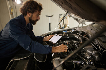 A skilled mechanic inspects a car engine while using a tablet to conduct a diagnostic test. The workshop is clean and organized with various tools in the background.