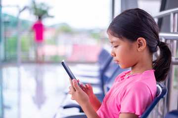 Young Girl Sitting and Using a Smartphone in an Outdoor Waiting Area