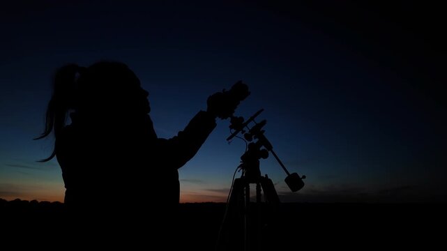 Amateur astro-photographer with a camera on a tripod photographing night sky with stars, planets, Moon and other celestial objects.