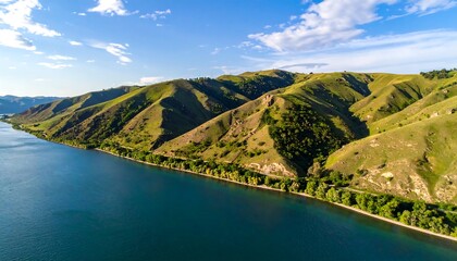 Rolling green hills meet tranquil blue water under a partly cloudy sky, creating a serene natural vista