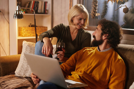 A couple relaxes on a sofa, engaging in a lively conversation while enjoying a glass of wine. They share smiles and laughter during a cozy indoor evening together.